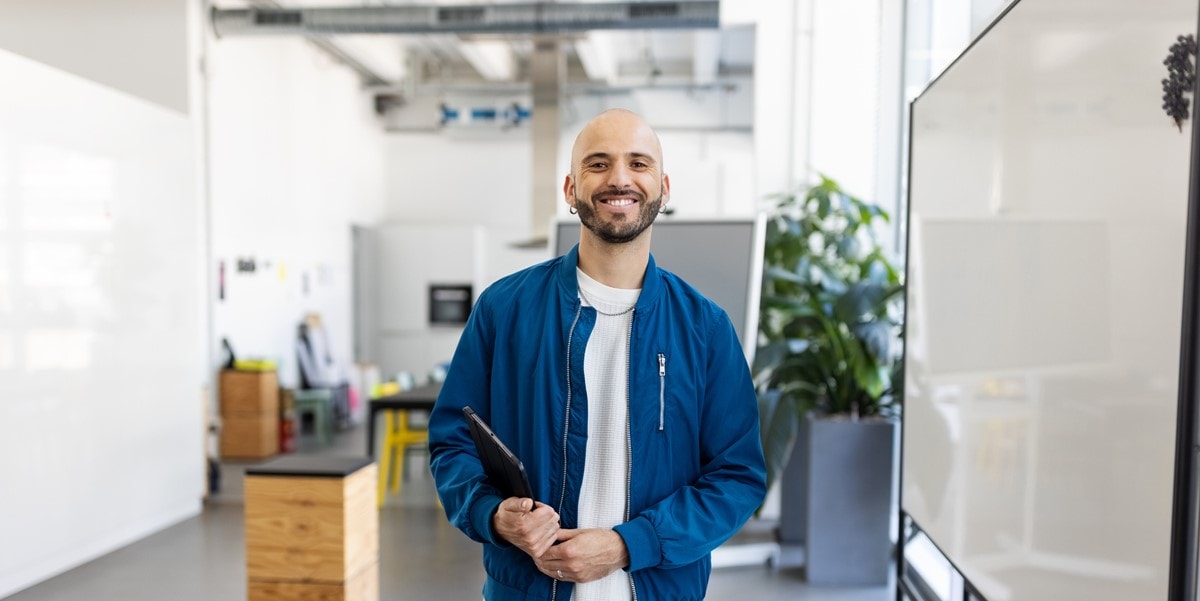 man in office smiling, holding laptop