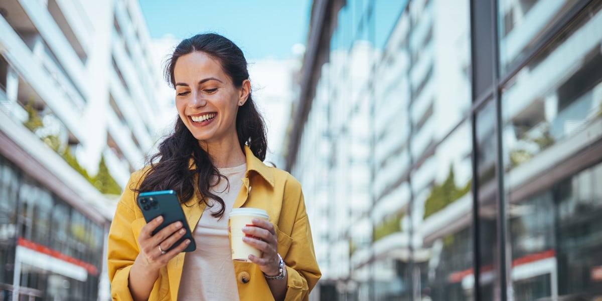 woman in city with phone and coffee cup